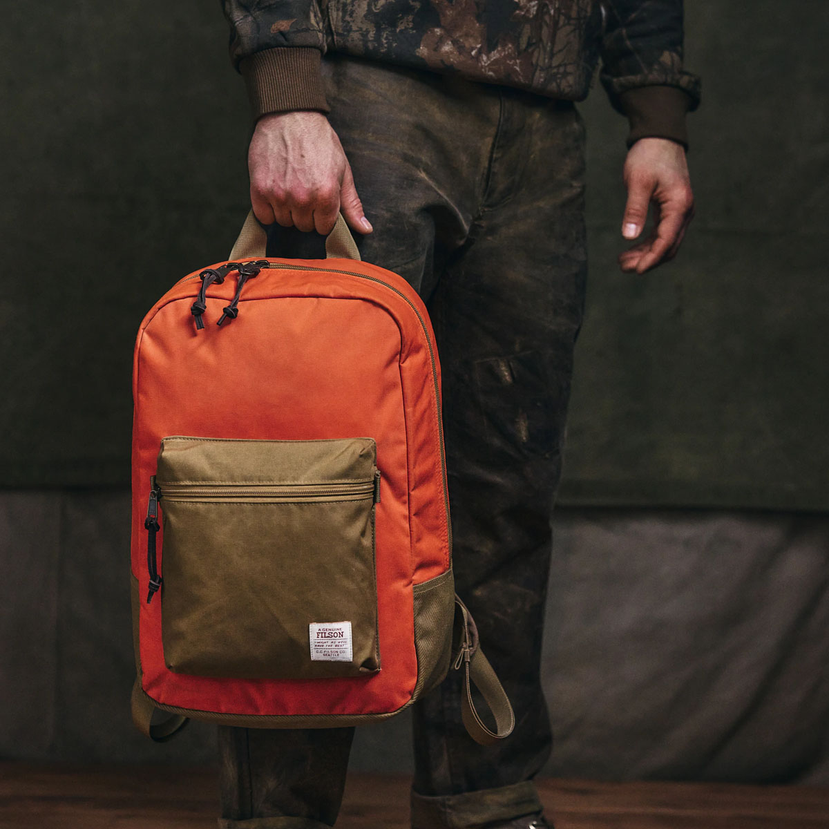 Filson Surveyor 25L Backpack Dark Tan/Flame, carried by the handle